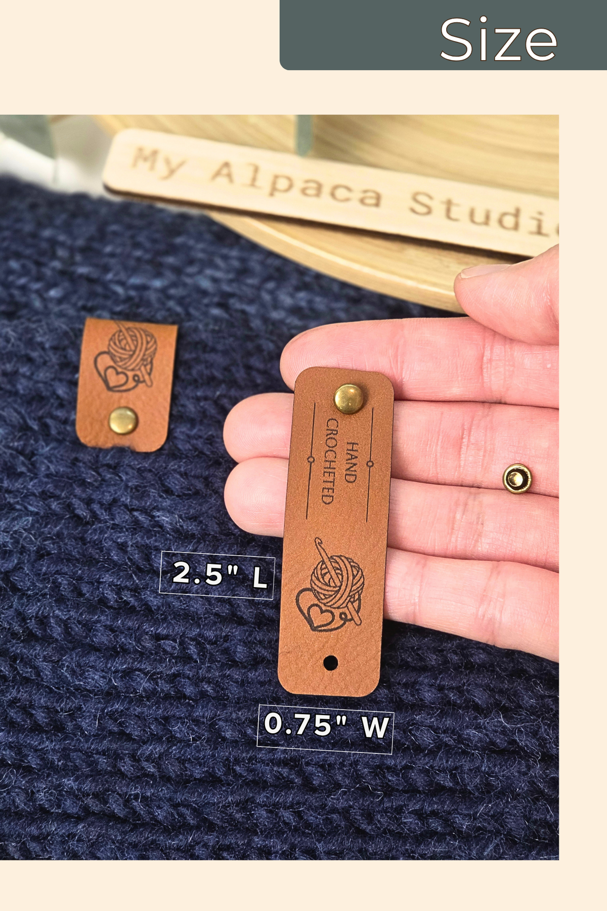 A close-up of a hand holding a brown leather garment size label that reads 'HAND CLOTHING' with a knitting motif, next to a matching smaller label on a navy knitted fabric. The image includes a 'Size' banner at the top and measurement labels '2.