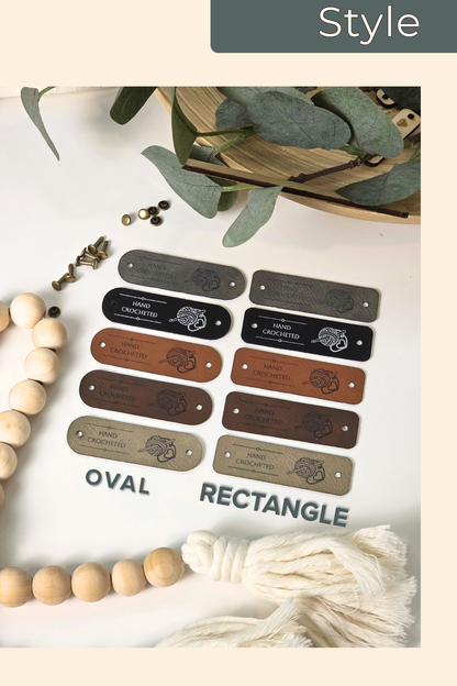A styled flat-lay showing engraved vegan leather tags in oval and rectangle shapes, displayed on a white surface with decorative beads, eucalyptus leaves, and a cream tassel. The top right corner includes a 'Style' label.