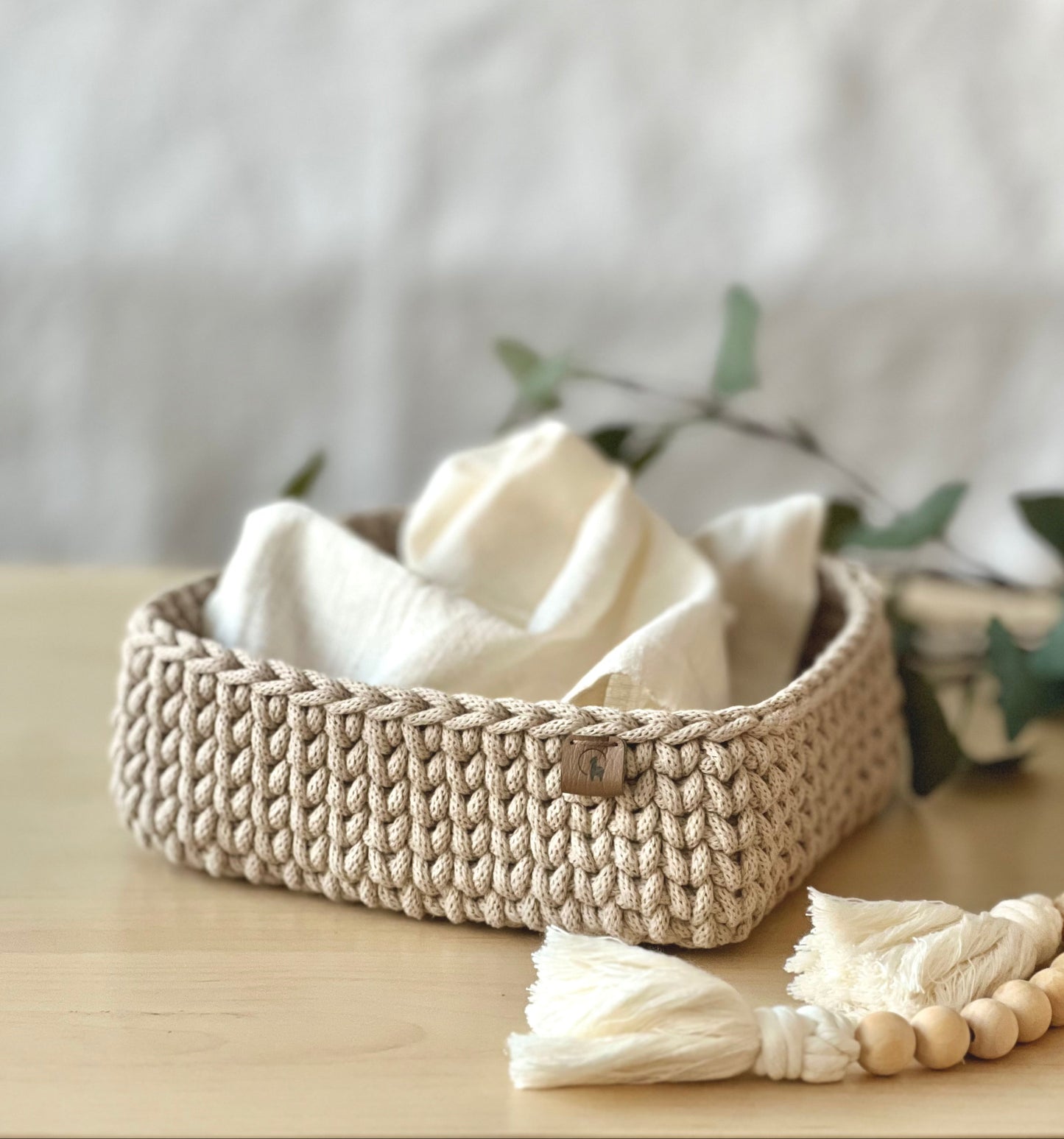 Two hand-crocheted square basket in beige, made from cotton with vegan leather tags, displayed on a wooden surface.