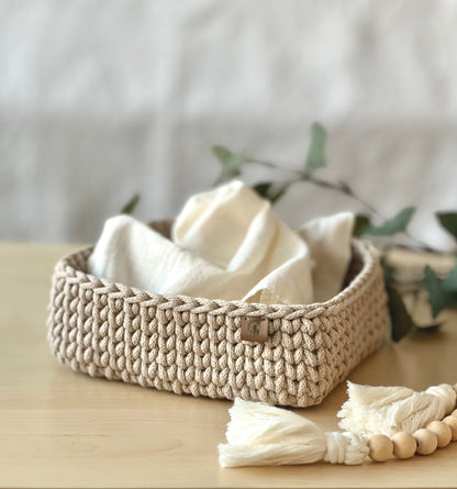 Two hand-crocheted square basket in beige, made from cotton with vegan leather tags, displayed on a wooden surface.
