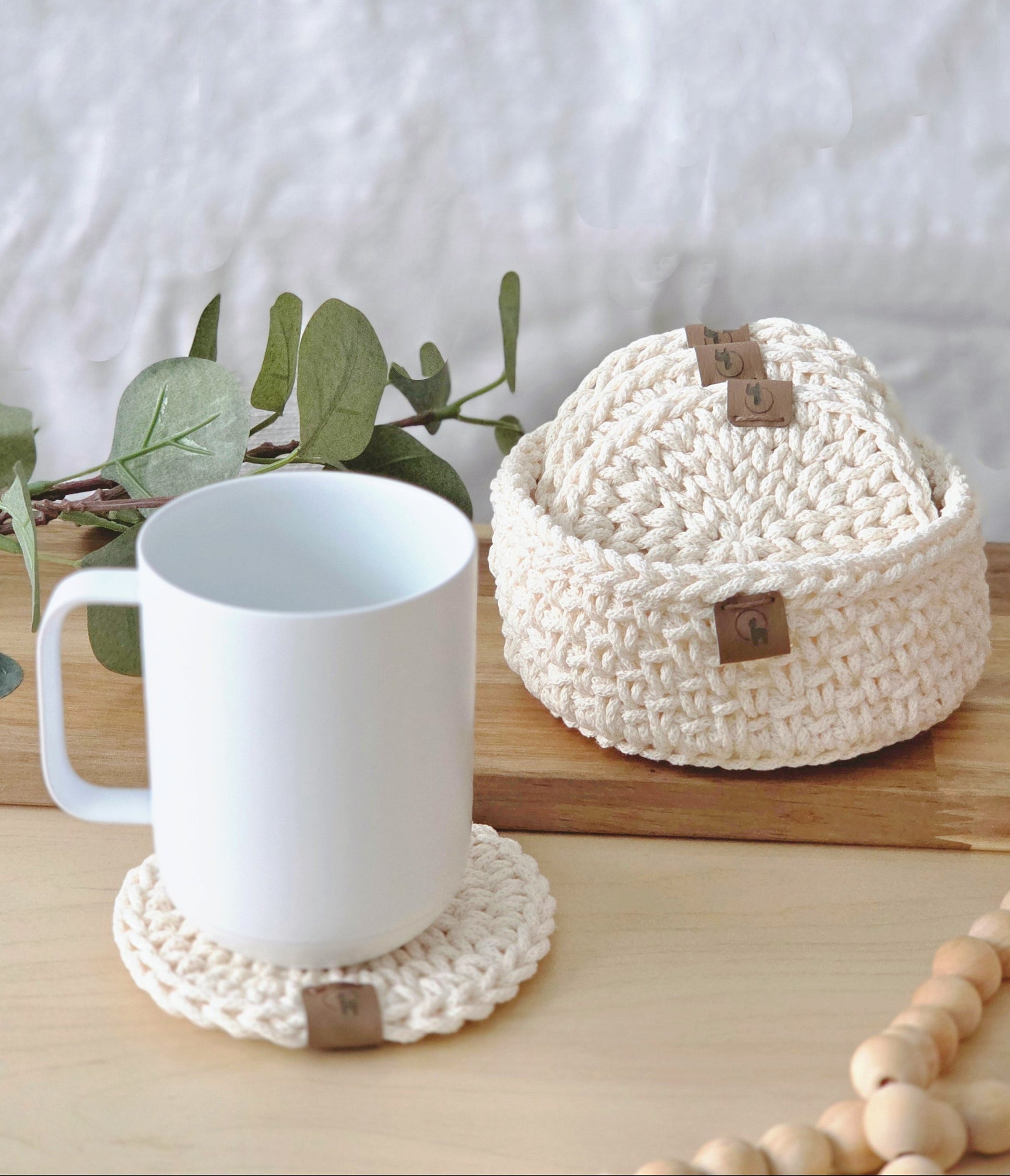 White mug on a woven coaster with a woven basket and greenery in the background