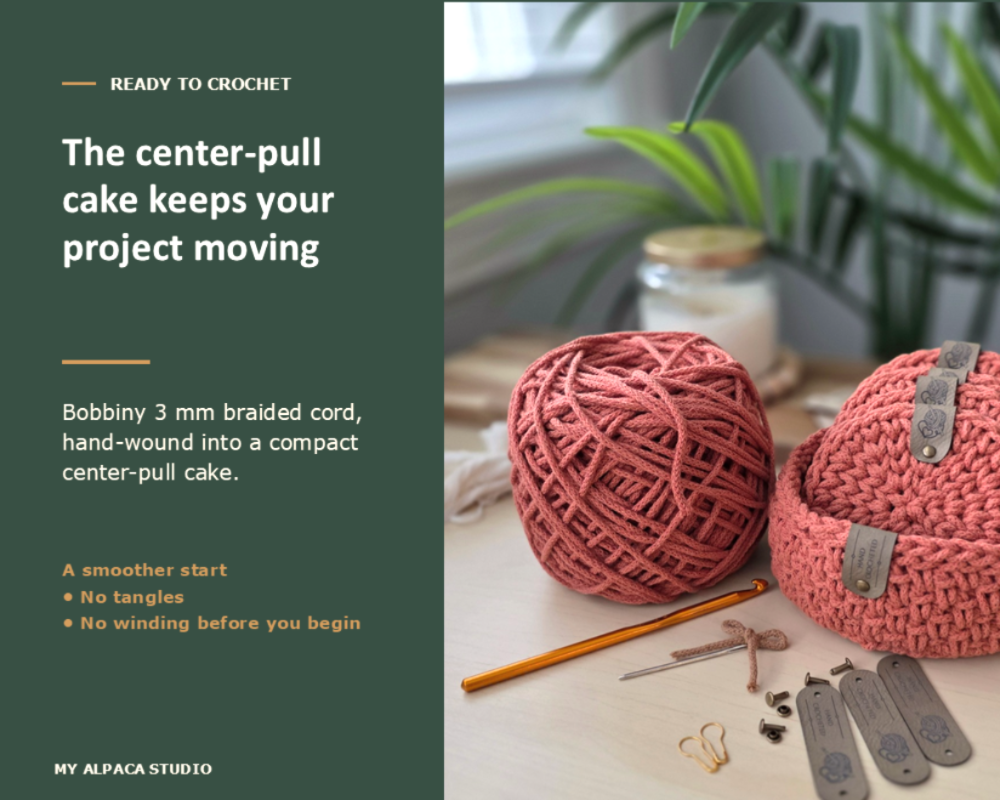 Promotional graphic for a crochet center-pull cake, showing a finished pink crocheted cake with a center pull tab, a ball of yarn, a crochet hook, and other crochet tools on a light wood surface. The left side has a dark green text panel explaining the product benefits, with the brand name 'MY ALPACA STUDIO' at the bottom.